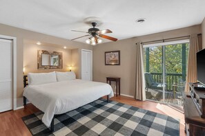 Une chambre à coucher avec un lit, un ventilateur de plafond, une fenêtre avec des rideaux, une petite table et un téléviseur.