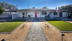 Une maison de plain-pied avec une porte rouge, un porche abrité et une pelouse bien entretenue.