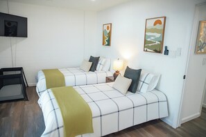 Quarto de hotel com duas camas, uma televisão fixada na parede e obras de arte acima das camas.