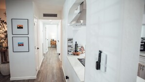 Un couloir avec un plancher en bois, des murs blancs et des tableaux encadrés. Une porte donne accès à une autre pièce.