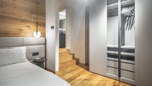 Une chambre moderne avec une tête de lit en bois, une table de chevet, une lampe suspendue et un dressing avec un miroir et des étagères.