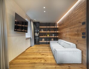 Ein modernes Interieur mit Holzboden, einem weißen Sofa, einer eingebauten Regaleinheit und einem an der Wand montierten Fernseher.