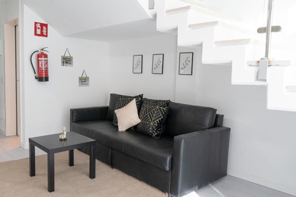 A modern living room with a black leather sofa, a small black table, and a fire extinguisher on the wall.