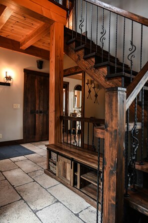 A wooden staircase with wrought iron railings, a stone-tiled floor, and a wooden door in the background. - Magic Chalet: Breathtaking River View, Spa in Les Éboulements (Les Éboulements)