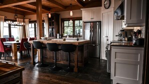 A modern kitchen with a central island, bar stools, and a dining area with red chairs. - Magique | Hot Tub & 360° St. Lawrence River View (Les Éboulements)