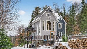 A two-story house with a balcony, surrounded by snow and trees. - Nature & Comfort Chalet on Lake Chapleau (La Minerve)