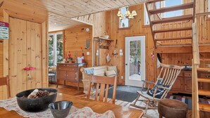 A cozy wooden cabin interior with a dining area, a rocking chair, and a staircase. - Nature & Comfort Chalet on Lake Chapleau (La Minerve)