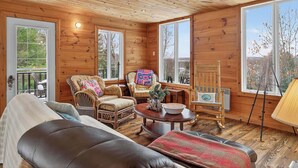 A cozy cabin interior with wooden walls, a large window, and a comfortable seating area with a sofa and chairs. - Nature & Comfort Chalet on Lake Chapleau (La Minerve)