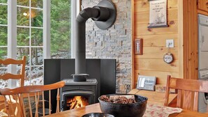 A cozy room with a wood-burning stove, a stone wall, and a wooden table with a bowl of wood chips. - Nature & Comfort Chalet on Lake Chapleau (La Minerve)