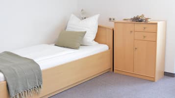 A single-bed room with a wooden bed, a bedside table, a small wardrobe, and a wall-mounted light fixture.