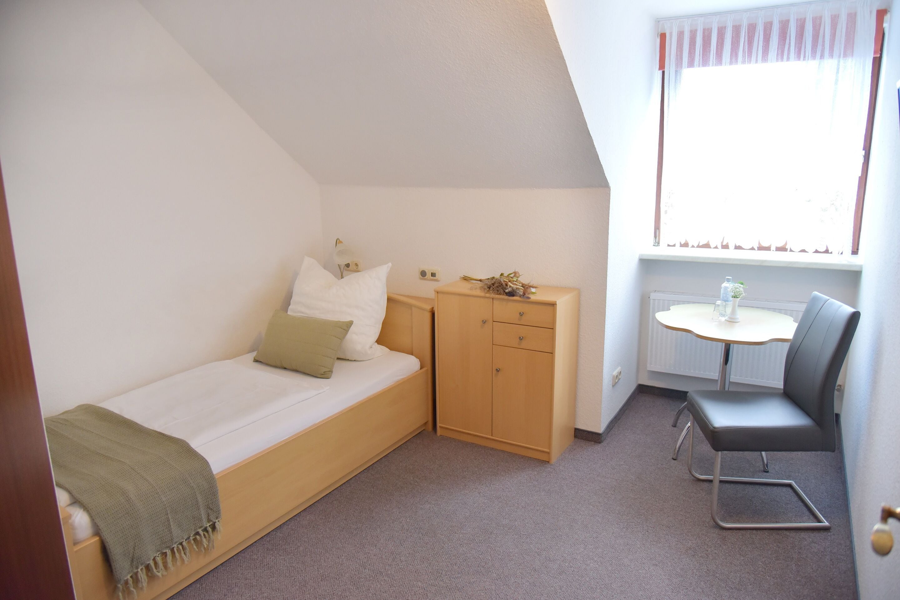 Une petite chambre avec un lit simple, une armoire en bois, une petite table et une chaise.