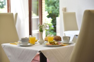 A breakfast table with two cups, a glass of orange juice, a muffin, and a plate of food.