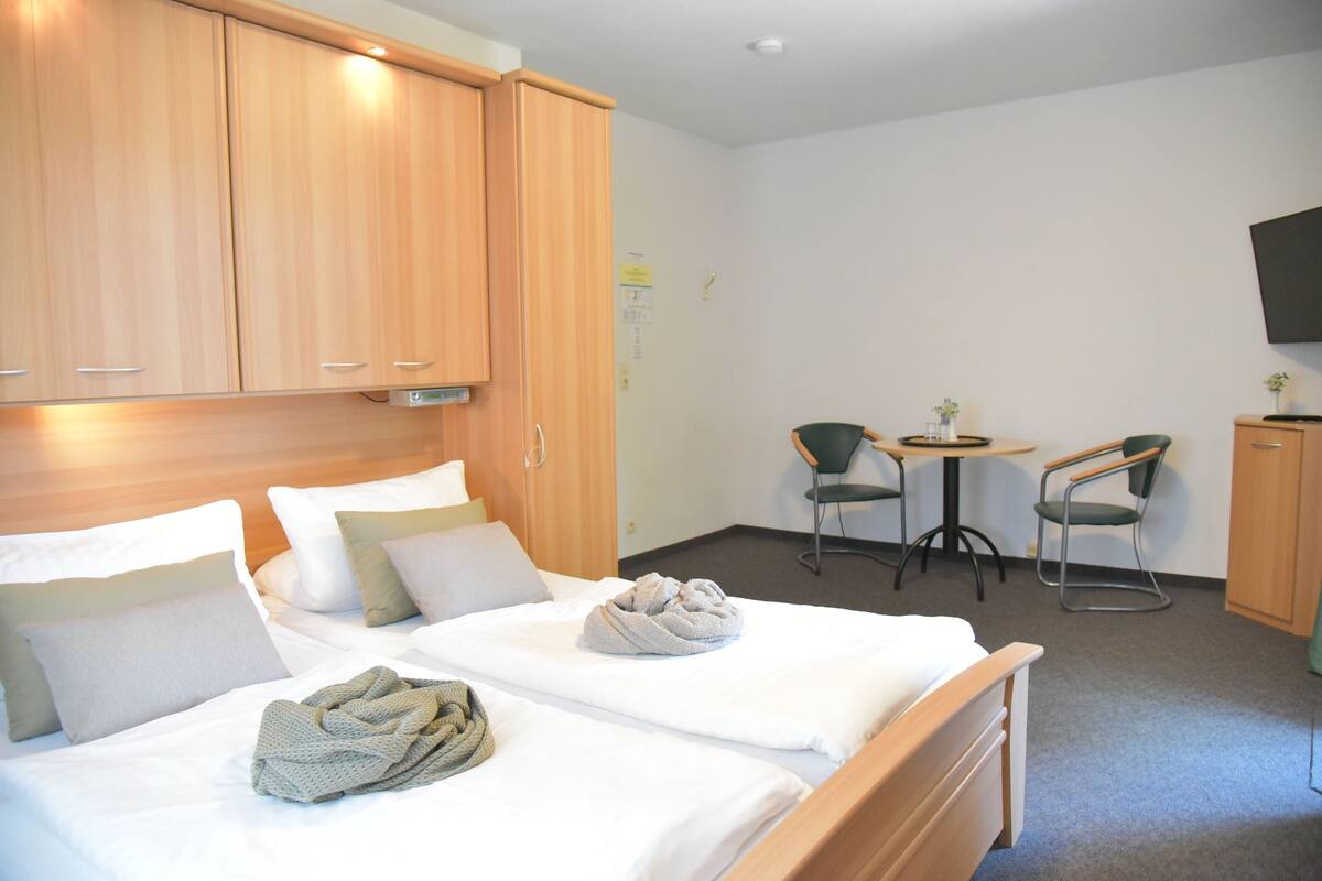 A hotel room with two beds, wooden cabinets, a small table with chairs, and a TV mounted on the wall.