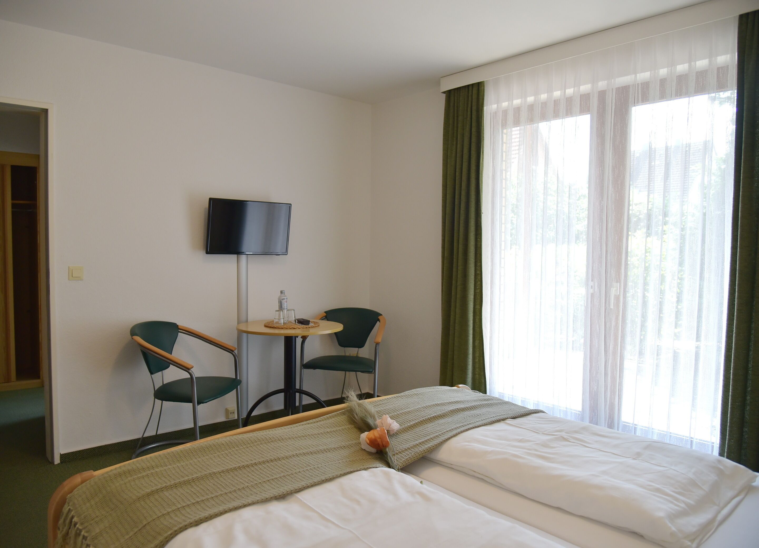A hotel room with a bed, two chairs, a small table, a television, and a window with curtains.