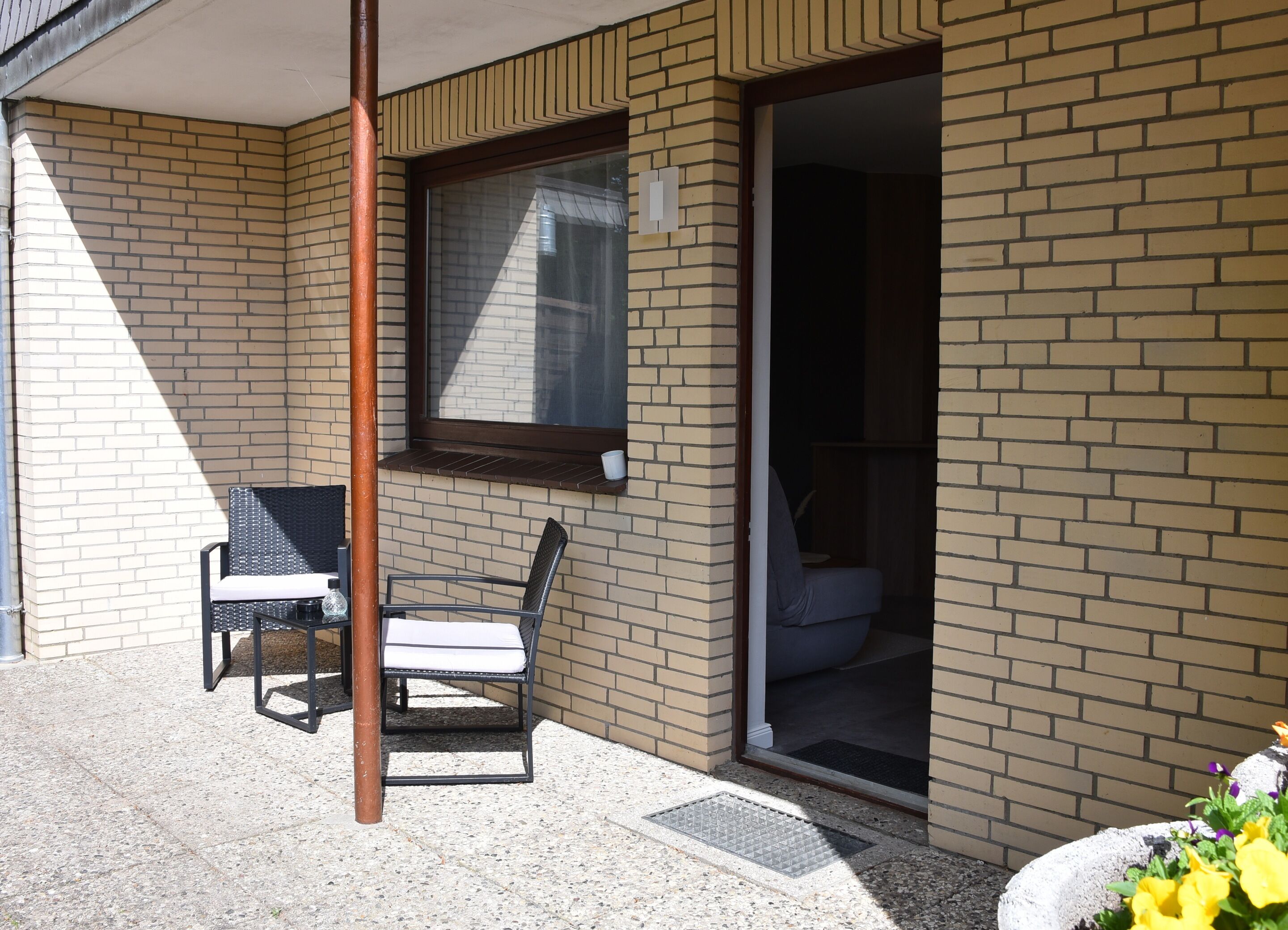 A corner of a building with a brick exterior, a window, and two chairs outside.