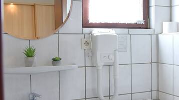 Une salle de bain avec un lavabo blanc, un miroir, une fenêtre ornée de rideaux en dentelle, un radiateur et des toilettes.