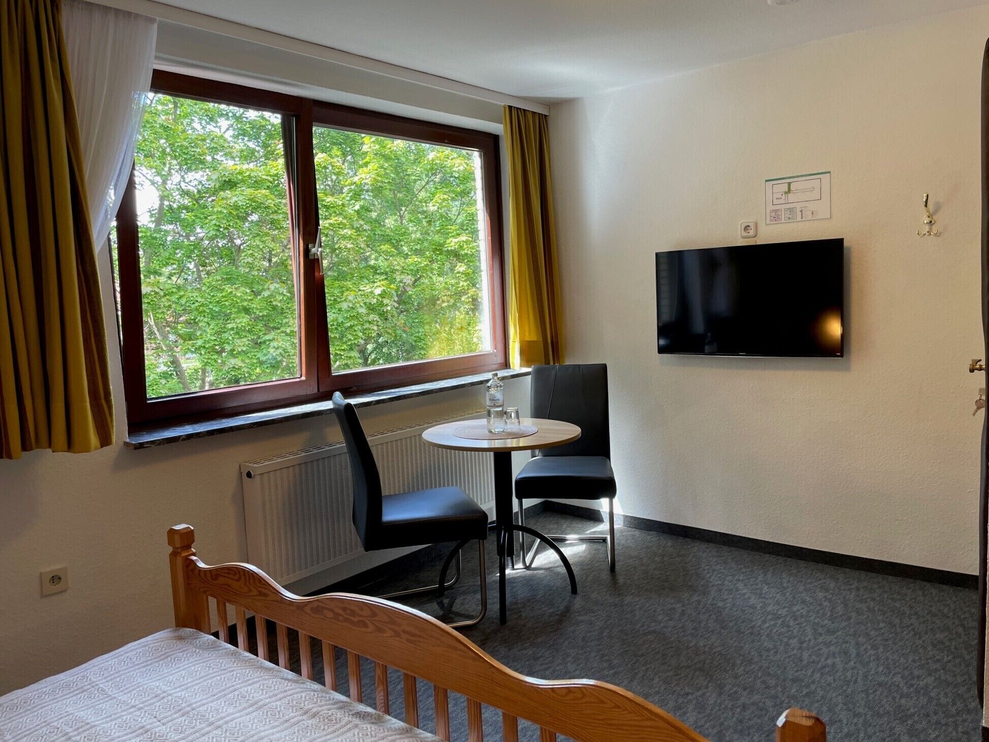 A hotel room with a bed, a round table with two chairs, a television on the wall, and a window with curtains.