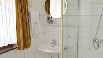 Un bany amb un lavabo blanc, un mirall, una cabina de dutxa de vidre i un radiador.