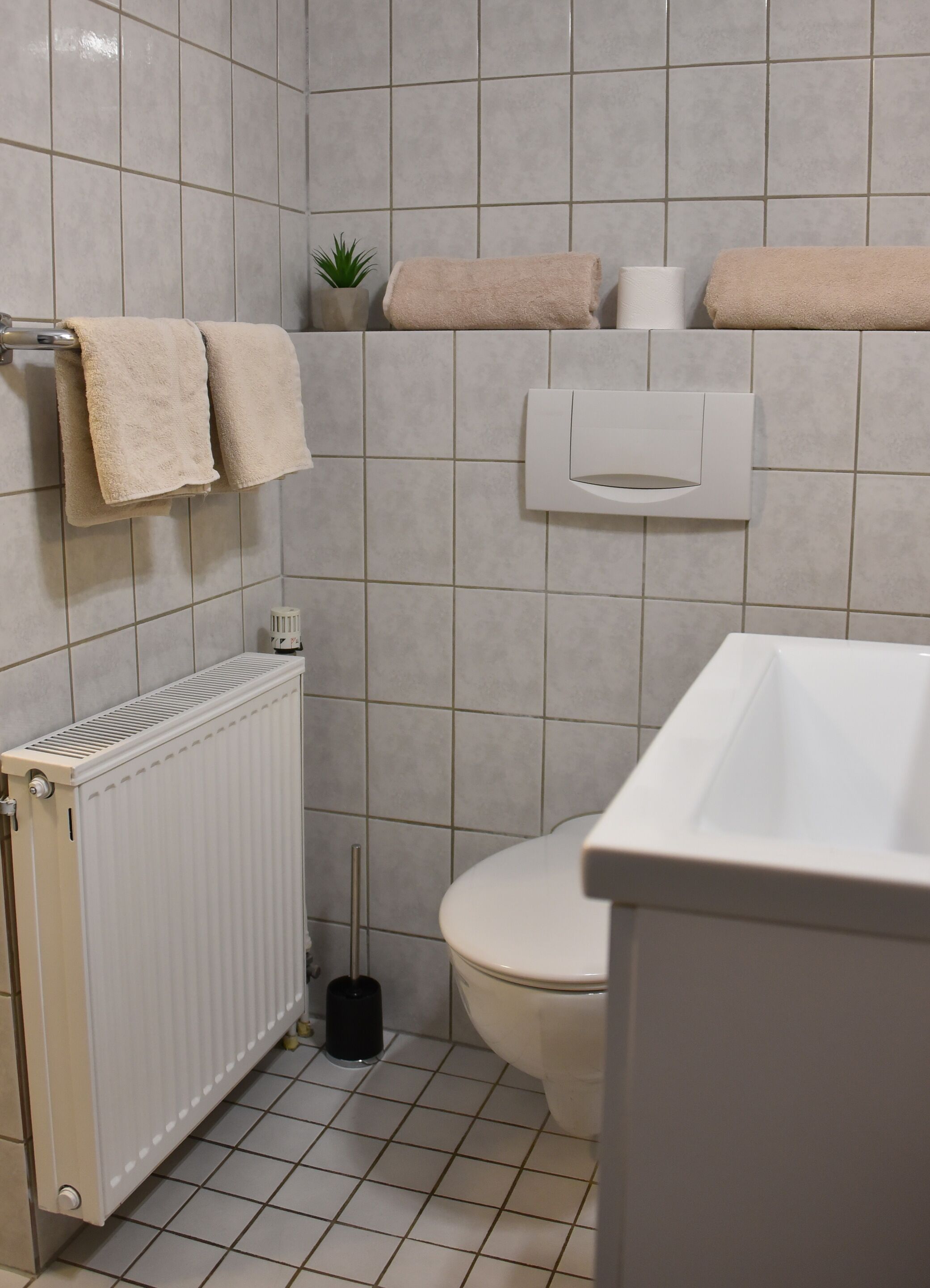 A bathroom with a toilet, a radiator, a sink, and two towels on a rack.