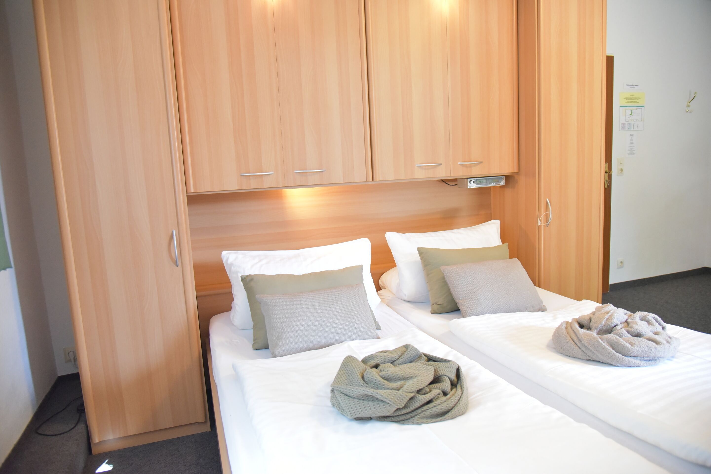 Una habitación de hotel con dos camas, un armario de madera y una manta sobre una cama.