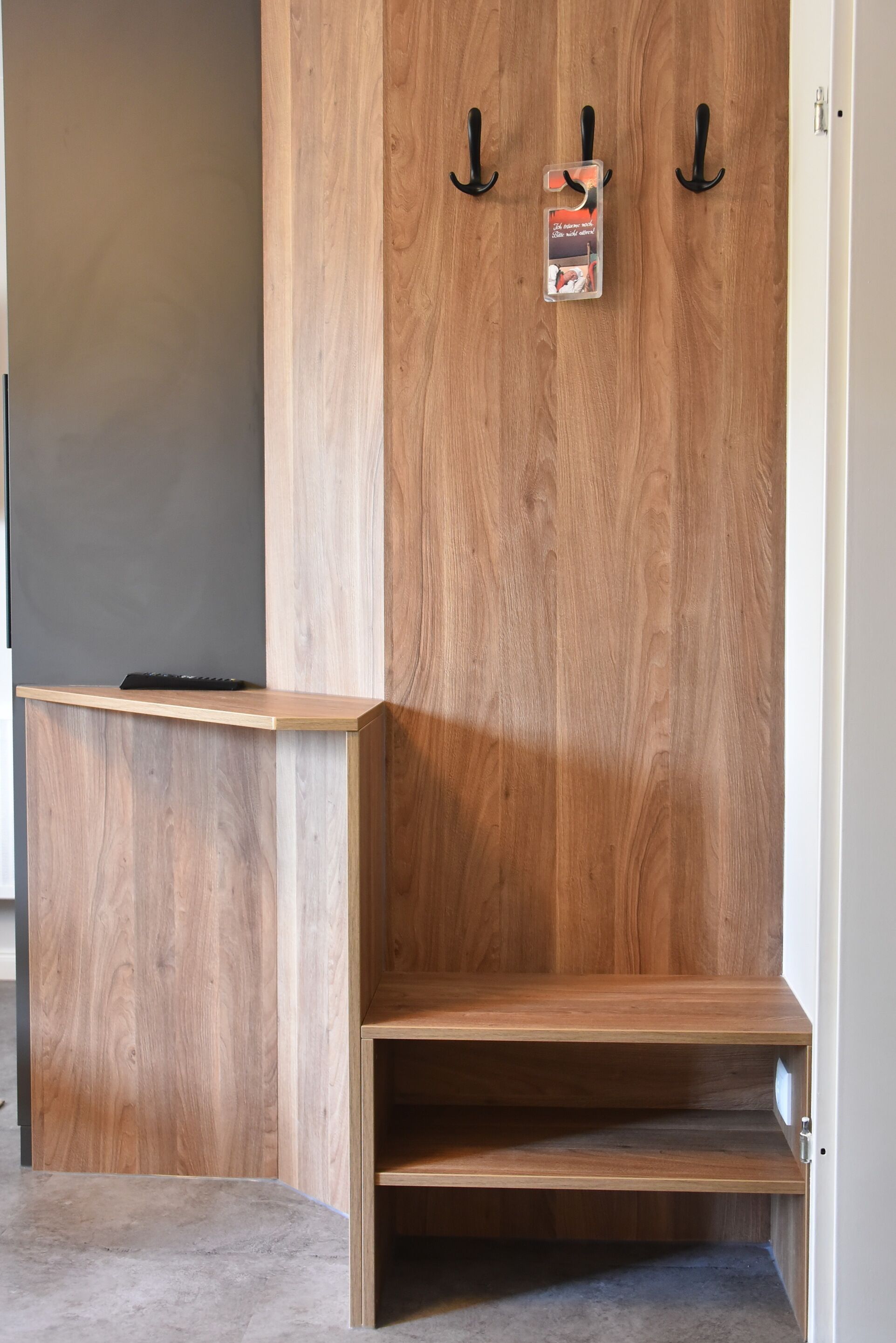 A wooden reception desk with a flat surface and a lower shelf, accompanied by three black hooks on the wall.