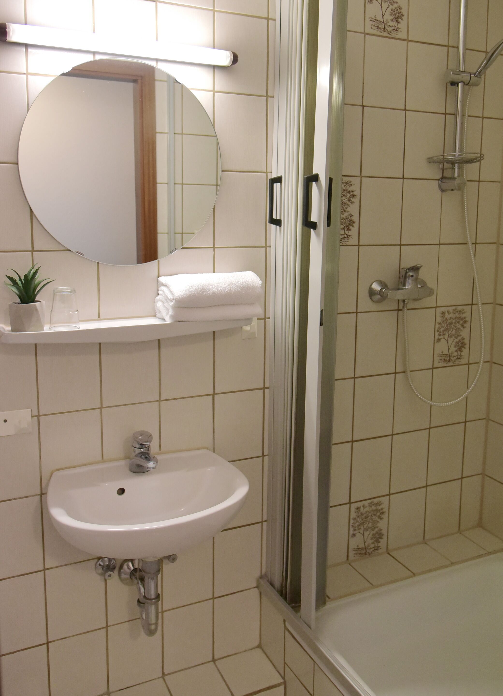 A bathroom with a sink, mirror, towel rack, shower, and decorative tiles.