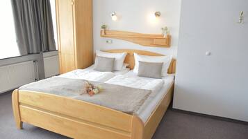 A neatly made bed with a wooden headboard, white bedding, and a decorative flower arrangement.