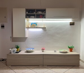 Une cuisine équipée d’un four à micro-ondes encastré, d’une étagère ornée d’objets décoratifs et d’un sol carrelé.
