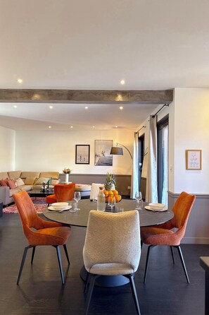 Un salon moderne avec une table à manger ronde, deux chaises orange et un canapé.