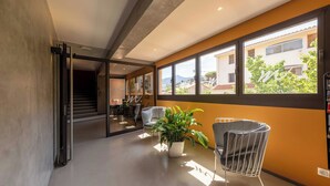 A modern interior with a staircase leading to another level, a seating area with chairs and a potted plant, and large windows offering a view of the outside. - Appartements Hôtel & Spa Le Madeloc Collioure Centre (Collioure)