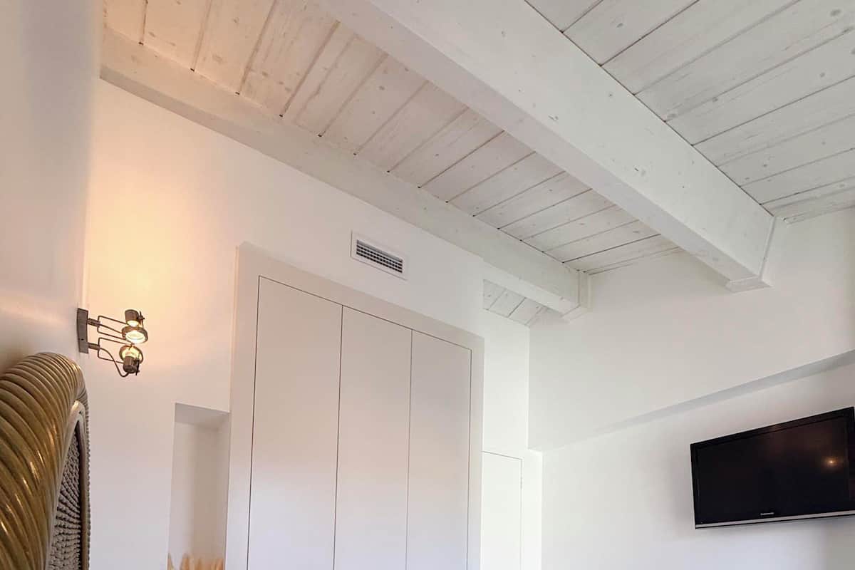 Een slaapkamer met een bed, een kledingkast, een televisie en een wandplank met decoratieve objecten.
