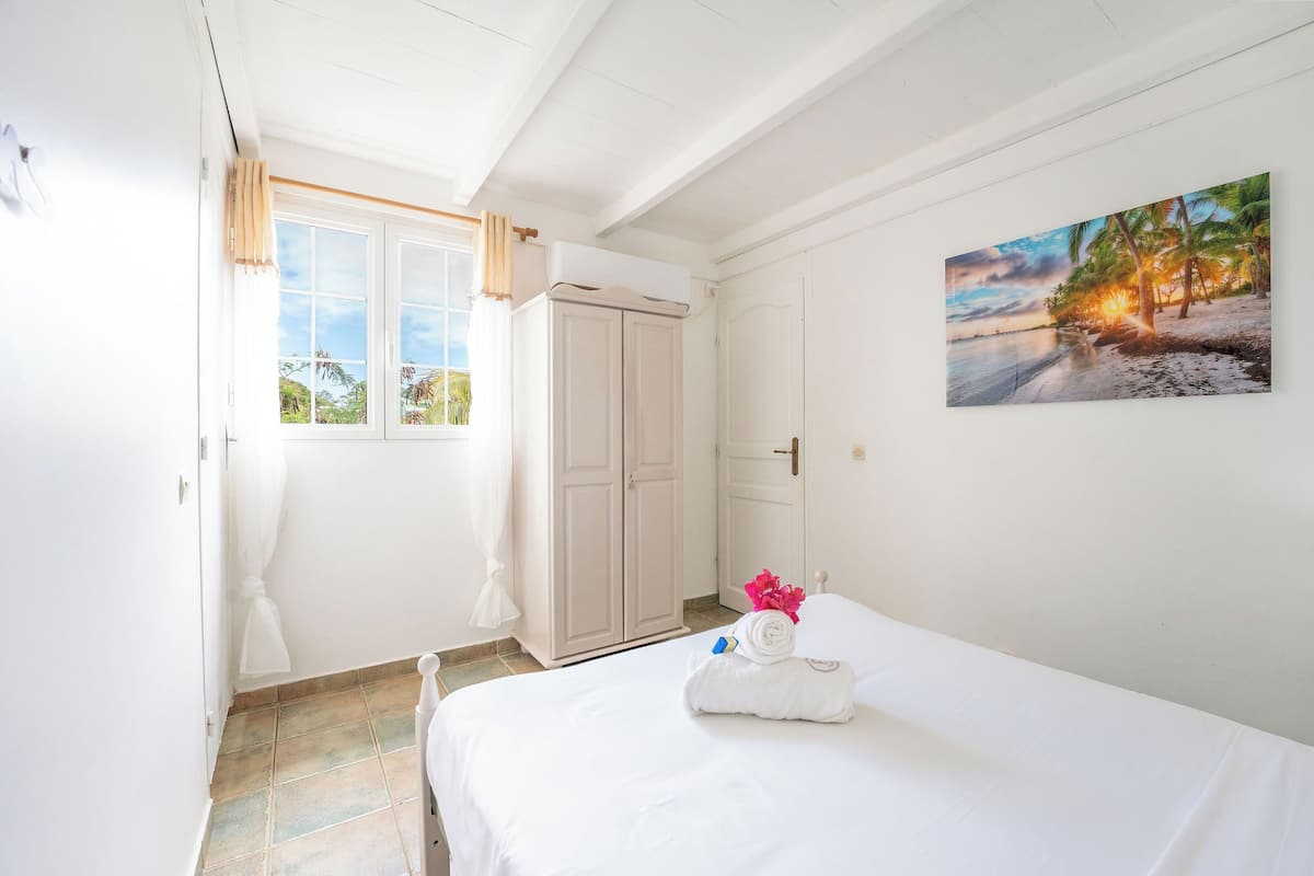 A hotel room with a bed, a painting of a beach scene, a wardrobe, and a window with curtains.