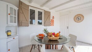 A dining area with a glass table, white chairs, a fruit basket, and a wall clock. - CASA LYDIE - ÉVASION CRÉOLE AVEC PISCINE (Saint-François)