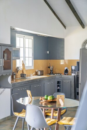 A modern kitchen with a built-in oven, a coffee maker, and a dining area with a glass table and chairs. - CASA LYDIE - SUITE PISCINE PRIVÉE (Saint-François)