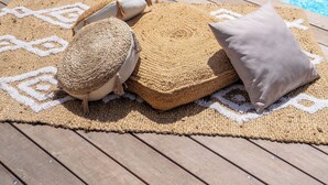 A wooden deck with a woven mat and a cushion, a pool with clear blue water, and a white fence in the background. - CASA LYDIE - SUITE PISCINE PRIVÉE (Saint-François)