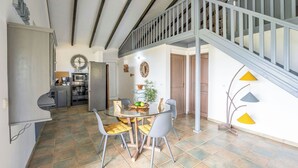 A dining area with a glass table and chairs, a kitchen in the background, and a staircase with a railing. - CASA LYDIE - SUITE PISCINE PRIVÉE (Saint-François)