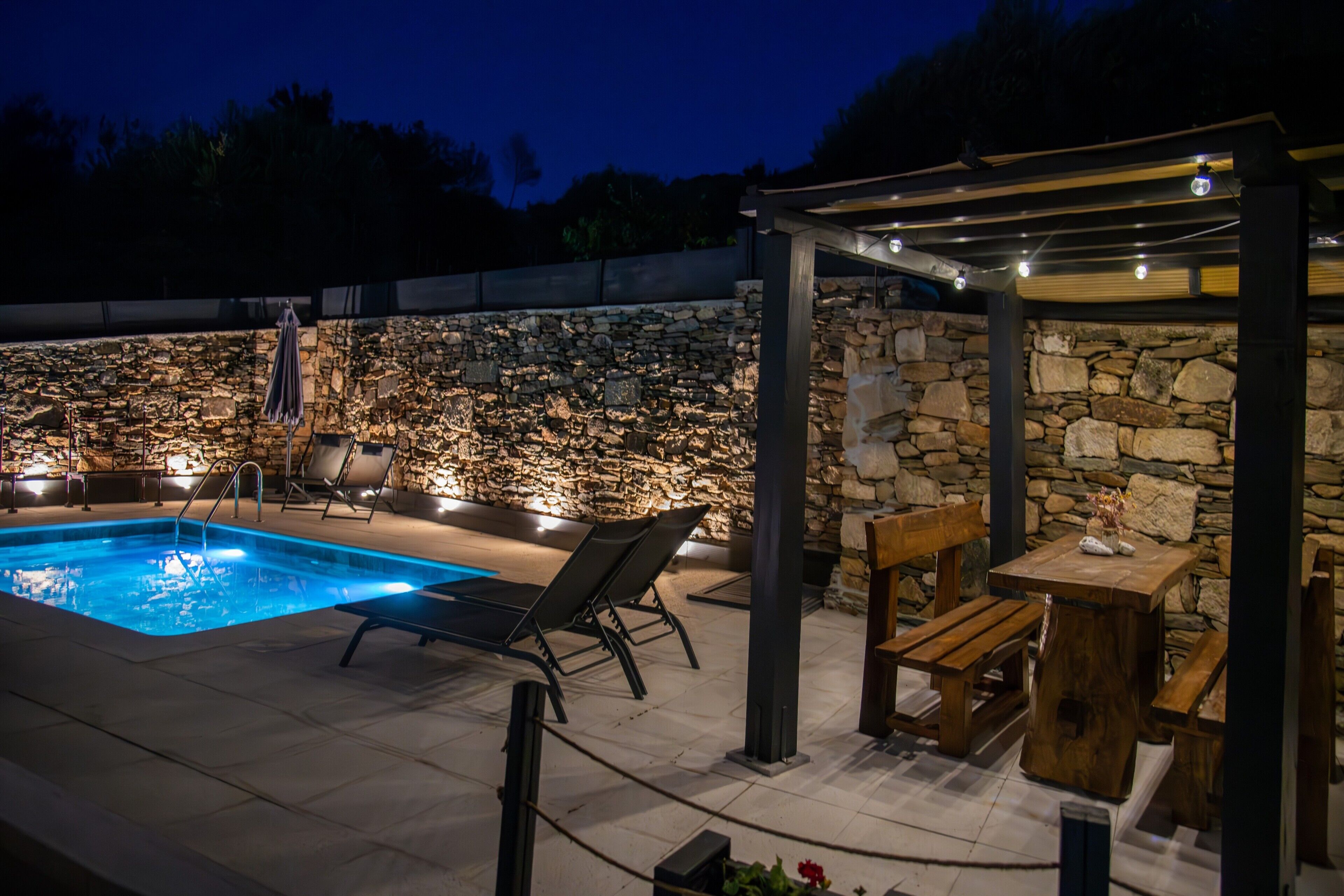 Una piscina con sillones de descanso y un muro de piedra.