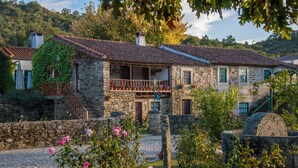 A stone building with a tiled roof, a wooden balcony, and a garden with pink flowers. - Country House 'Villa Jerusalém' with Mountain View, Wi-Fi & Air Conditioning (Romeu)