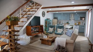 A living room with a staircase, a TV, a sofa, and a kitchen in the background. - Country House 'Villa Jerusalém' with Mountain View, Wi-Fi & Air Conditioning (Romeu)