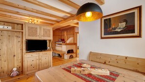Un interior de madera con una televisión, armarios de madera, una mesa de comedor con posavasos y un cuadro en la pared.