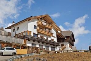 A multi-story building with wooden balconies, a car parked in front, and a clear sky.