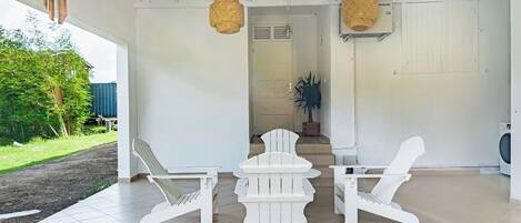 A covered outdoor area with white chairs and a table, a ceiling fan, and a washing machine in the background.