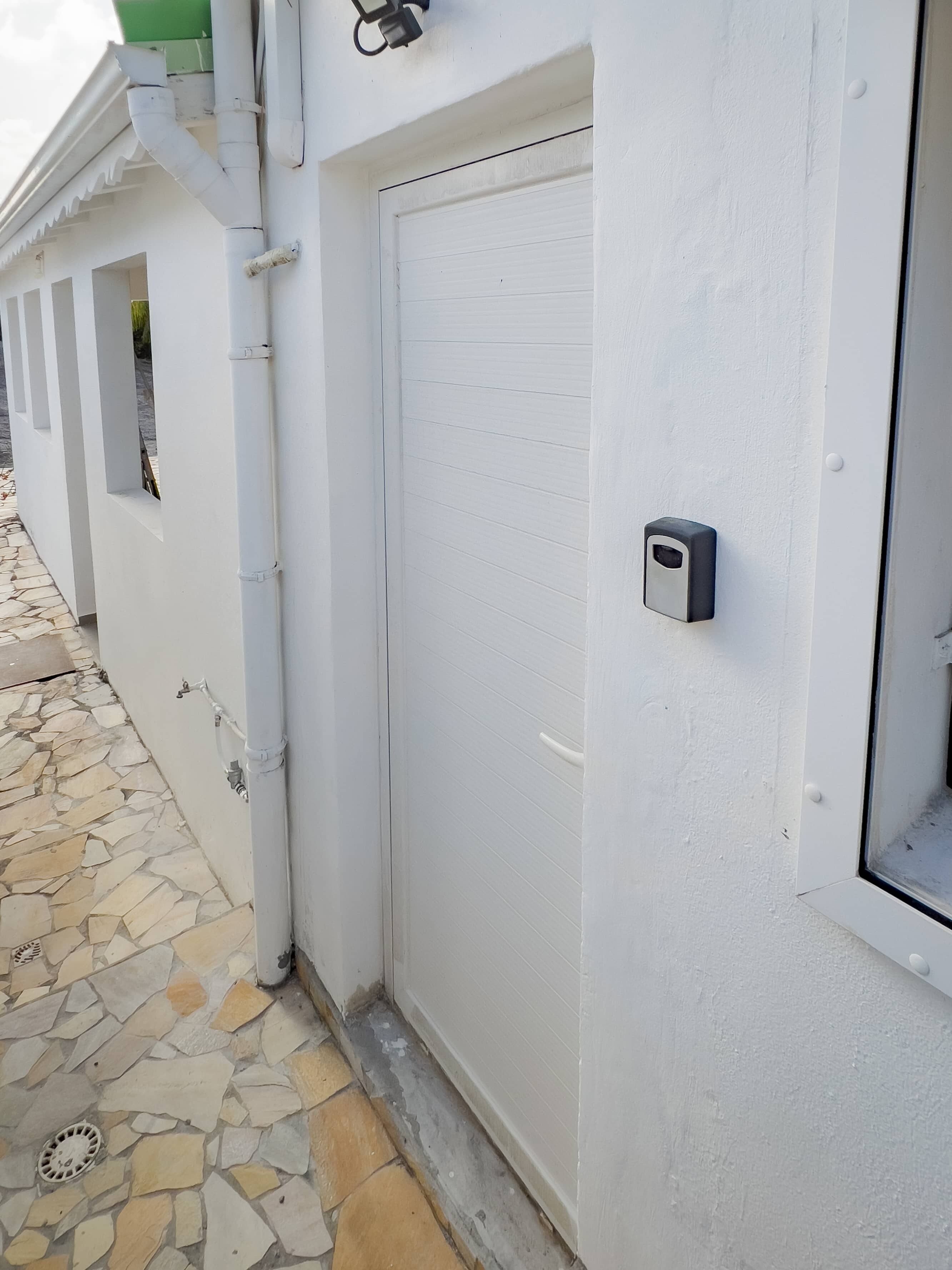 A white exterior wall with a closed door, a small window, and a security camera.