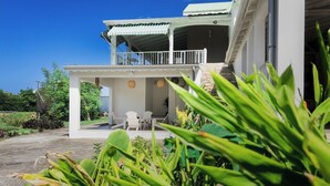 A two-story house with a balcony, outdoor seating, and lush greenery. - Habitation Yucca à 5 min de la plage (Le Moule)