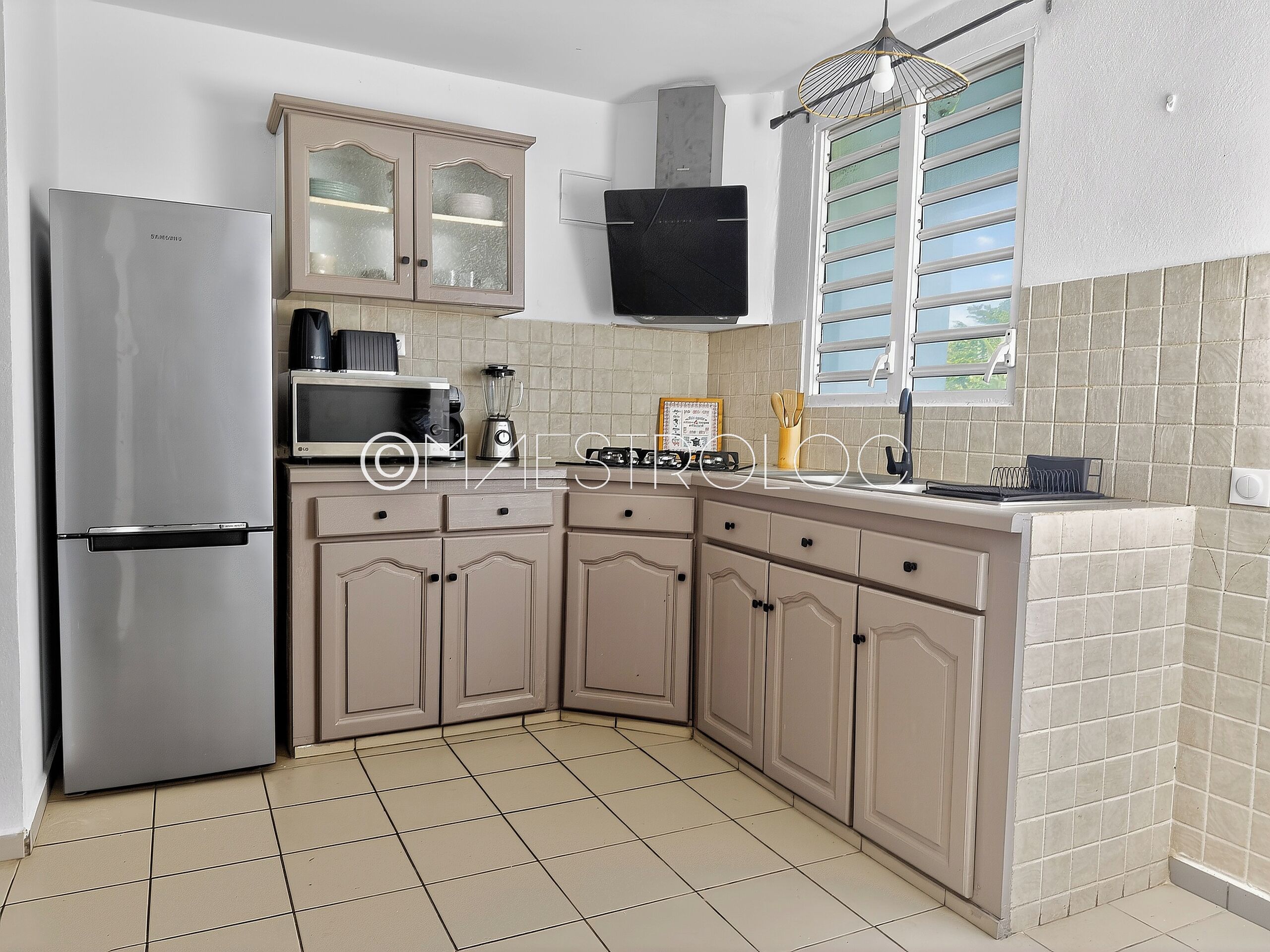 A kitchen with a stainless steel refrigerator, beige cabinets, a microwave, and a gas stove.