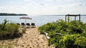 En strand med en rad solstolar, ett parasoll och en träkonstruktion.