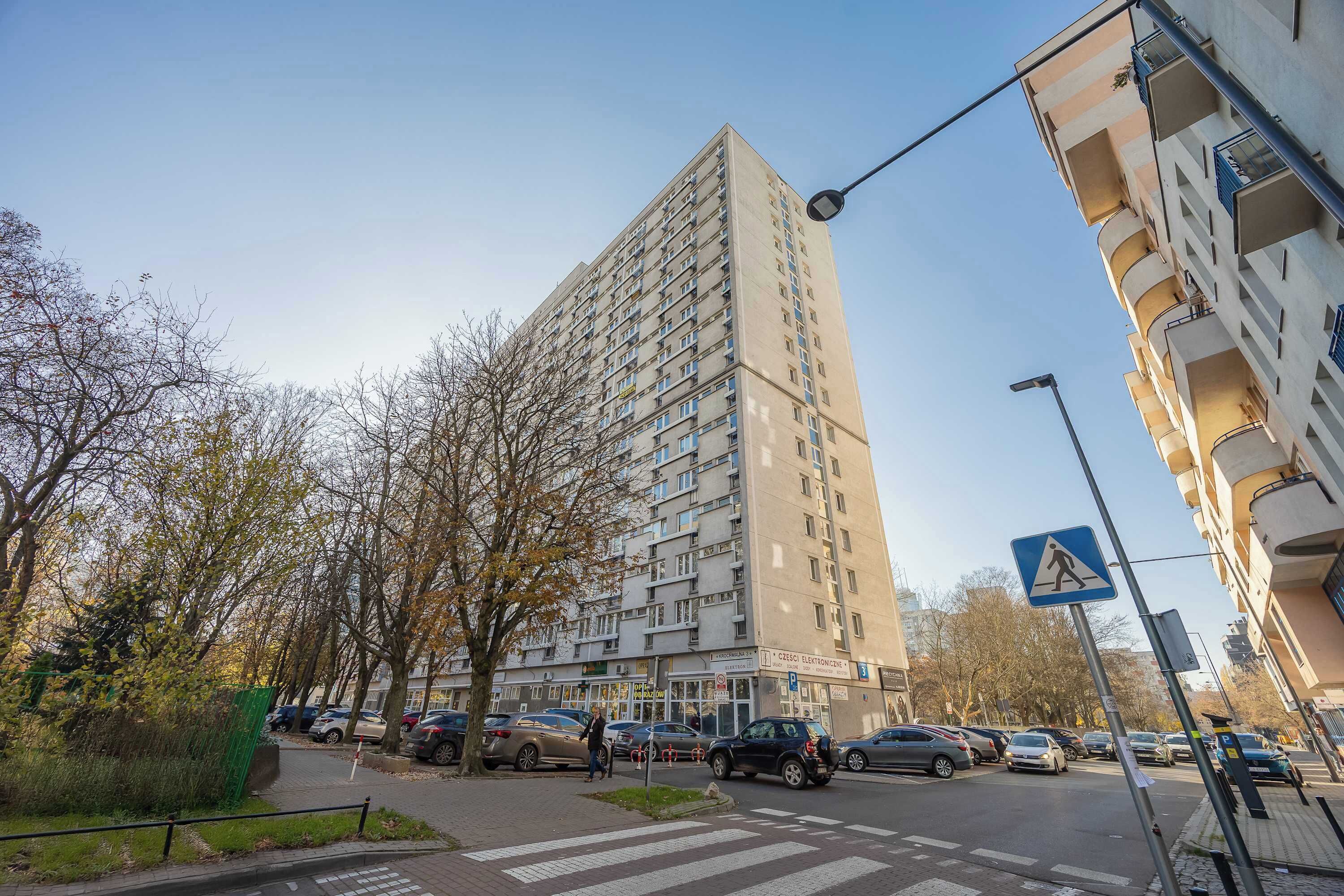 Een hoog appartementencomplex met meerdere balkons en een bord voor een voetgangersoversteekplaats.