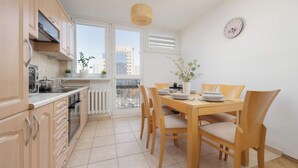 Una cucina moderna con mobili in legno, un tavolo da pranzo con sedie e vista sulla città attraverso ampie finestre.
