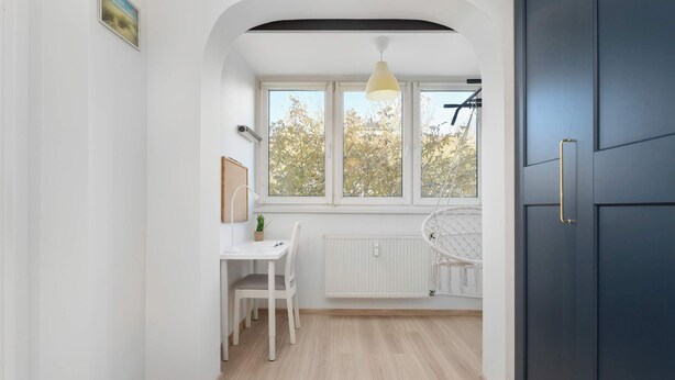 A modern kitchen with white cabinetry, a dining area with a white table and chairs, and a window with a view of trees. - Comfortable Apartment | Close to Old Town and Place to Work (Gdańsk)