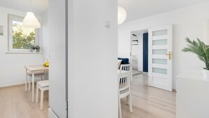 A bright, white room with a wooden floor, a dining table with chairs, a potted plant, and a door leading to another room. - Comfortable Apartment | Close to Old Town and Place to Work (Gdańsk)
